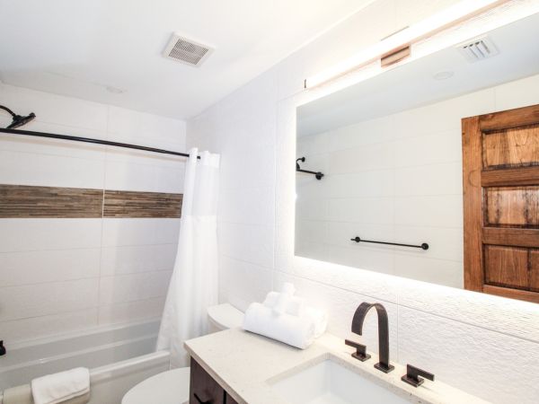 A modern bathroom with a bathtub, a white shower curtain, a large mirror above the sink, and wooden door accents.