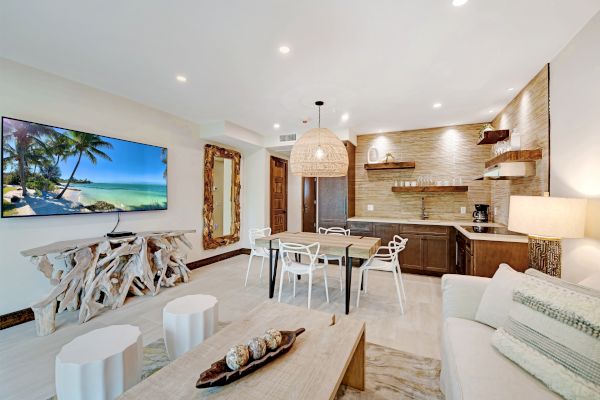 A modern living room with a large TV, unique wood furniture, a kitchen area, a dining table with chairs, and a cozy couch.