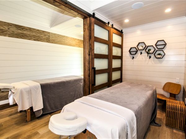 A modern, serene massage room with a massage table, wooden decor, shelves with small plants, and soft lighting in a cozy environment.