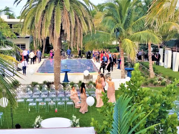 A lush outdoor setting features a pool, chairs, guests in formal attire, and large "LOVE" letters, indicating a wedding or event.