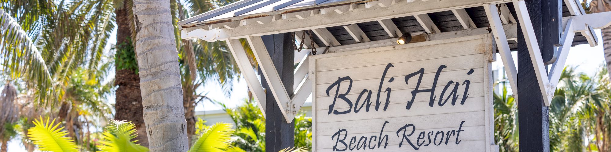 The image shows a signboard for "Bali Hai Beach Resort" set against a backdrop of palm trees and tropical foliage.